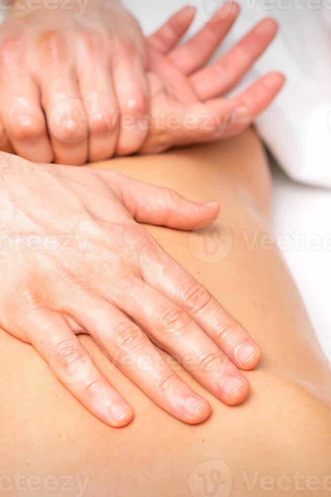 A male physiotherapist stretches the arms on the back of a man lying down, close up. photo