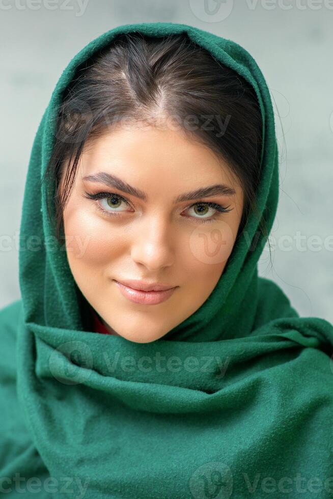 retrato de un bonito joven caucásico mujer con maquillaje en un verde Pañuelo en gris antecedentes. foto