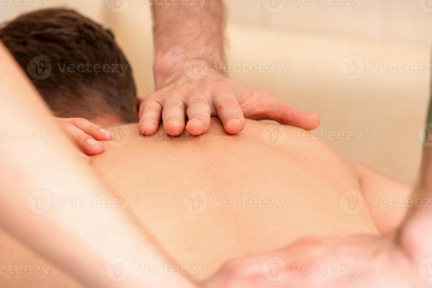 Young man receiving back massage in four hands in spa beauty salon. photo