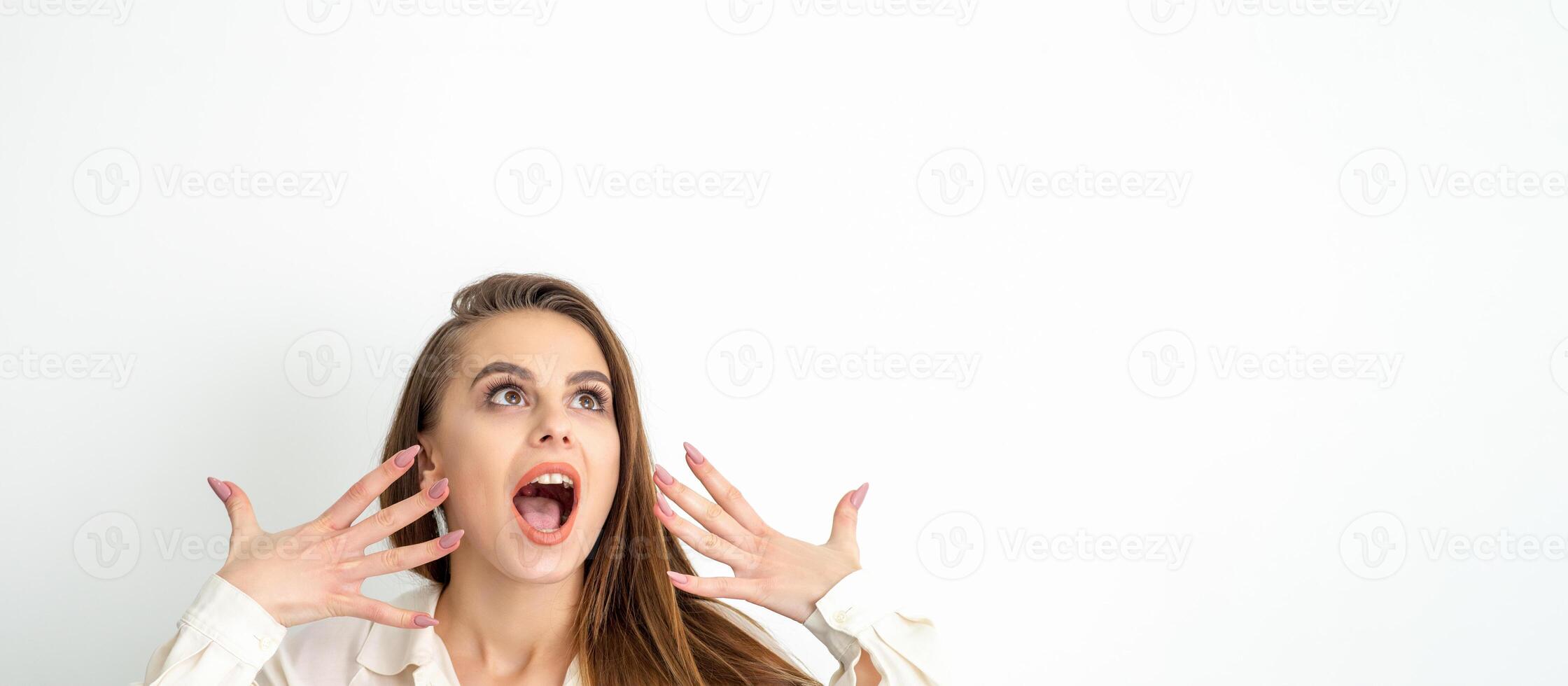 Shocked young caucasian woman with open mouth looking up and expresses surprise isolated over white background. Beautiful surprised brunette woman in studio. photo