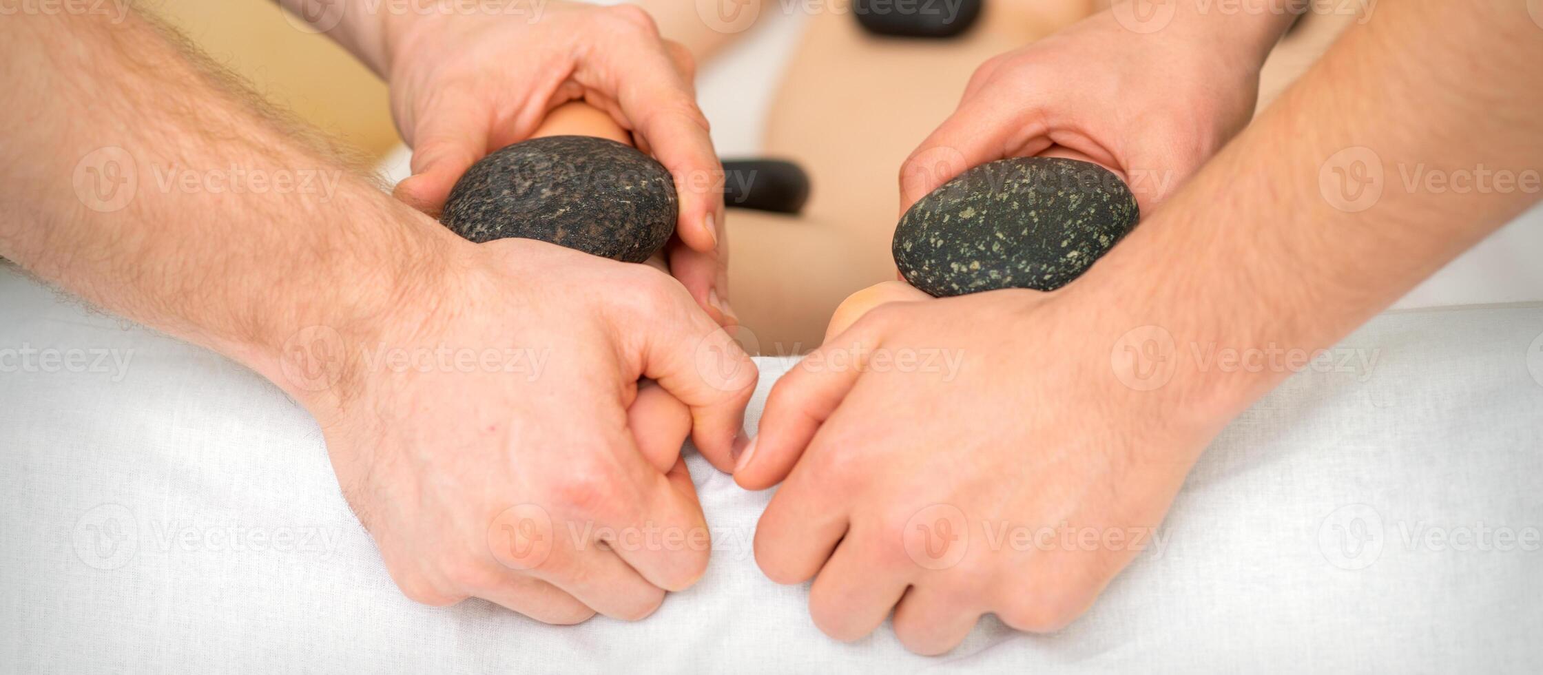 Two masseurs make a foot massage with a hot stone in four hands at the spa. photo