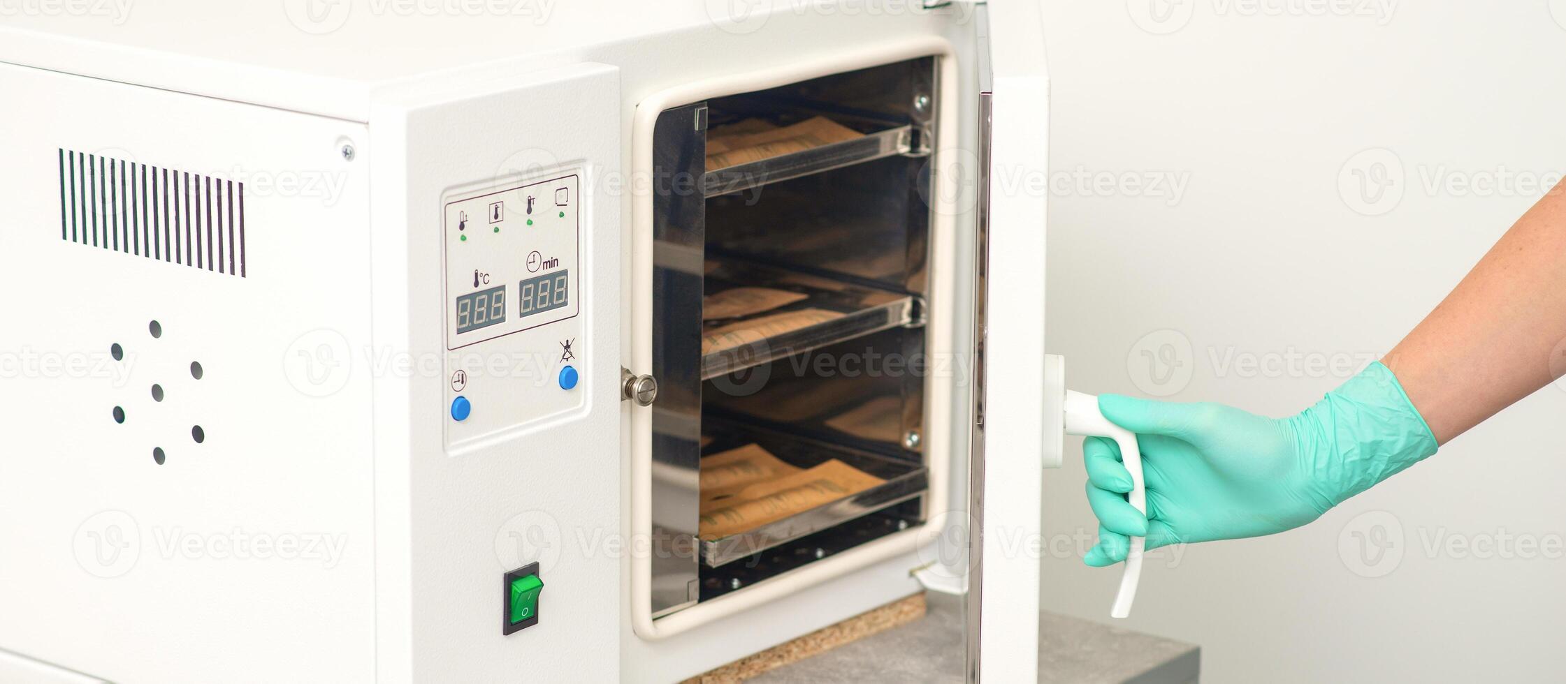 Beautician in protective gloves close the door of the machine for disinfection of tools before the depilation procedure. photo