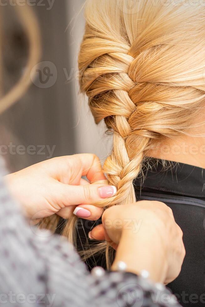 Braiding braid. Hands of female hairdresser braids long braid for a blonde woman in a hair salon. photo