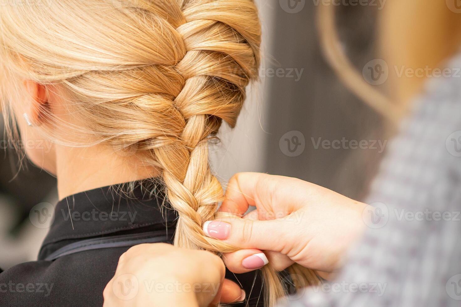 Braiding braid. Hands of female hairdresser braids long braid for a blonde woman in a hair salon. photo