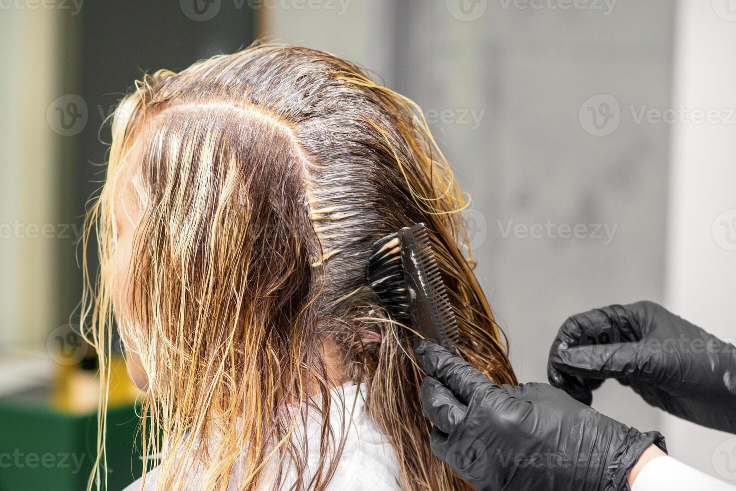 A hairdresser in black gloves is applying brush color to the hair of a customer. Hair coloring in a beauty salon close-up. photo