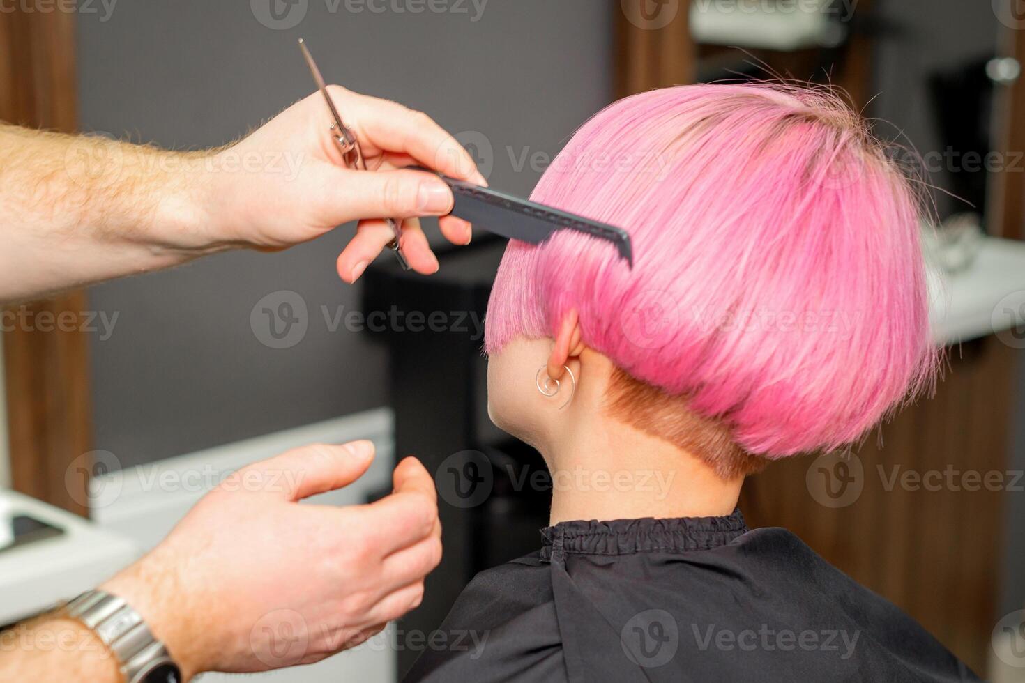 manos de peluquero peinada pelo haciendo corto rosado peinado para un joven caucásico mujer en un belleza salón. foto