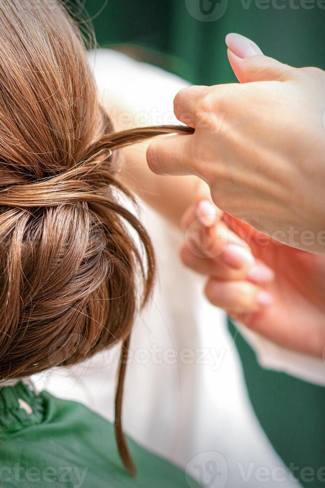 Professional hairdresser doing hairstyle for a beautiful brunette young woman with long hair. Concept of fashion and beauty. photo