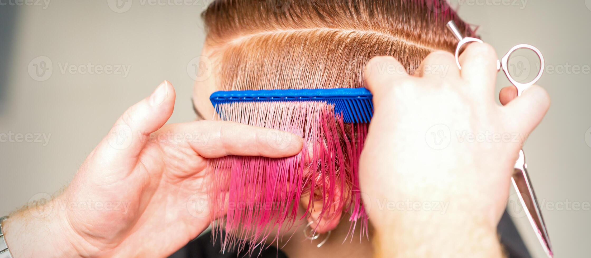 manos de peluquero peinada pelo haciendo corto rosado peinado para un joven caucásico mujer en un belleza salón. foto