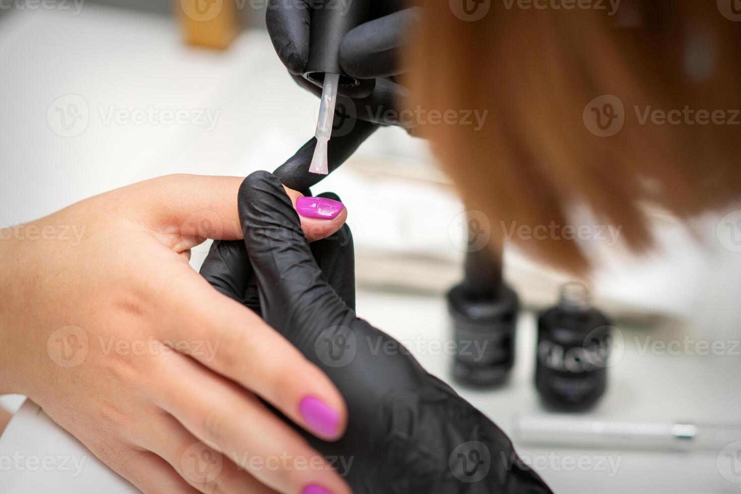 Painting nails of a woman. Hands of Manicurist in black gloves applying pink nail polish on female Nails in a beauty salon. photo