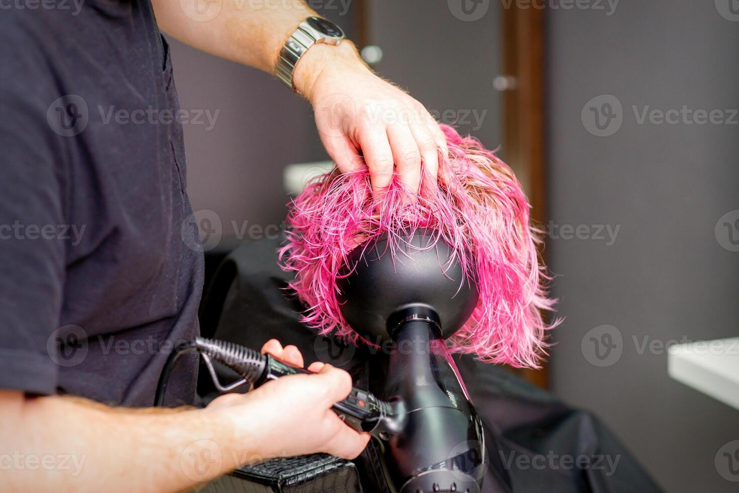 Hair Stylist making hairstyle using hair dryer blowing on wet custom pink hair at a beauty salon. photo
