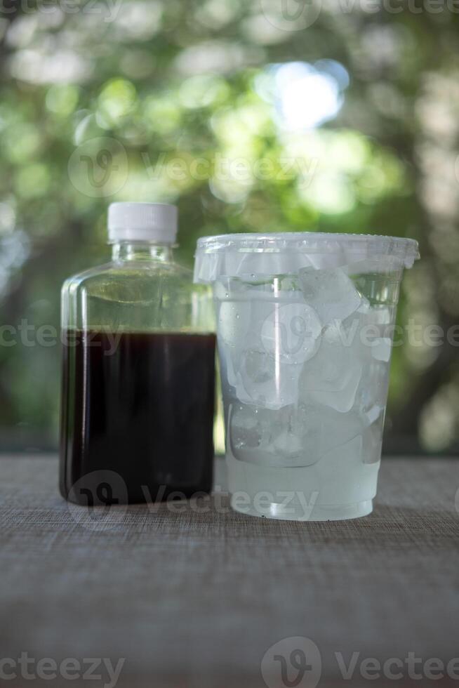 Black coffee in plastic bottle with plastic take away cup with ice cubes. photo