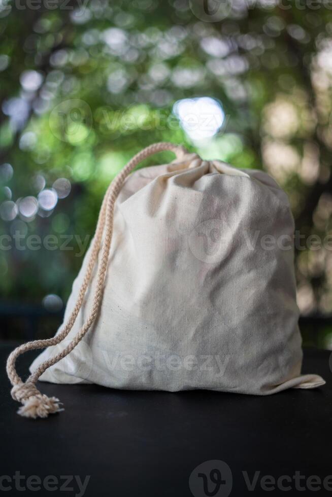 White drawstring pouch made of canvas fabric is placed on top of a table against nature background photo