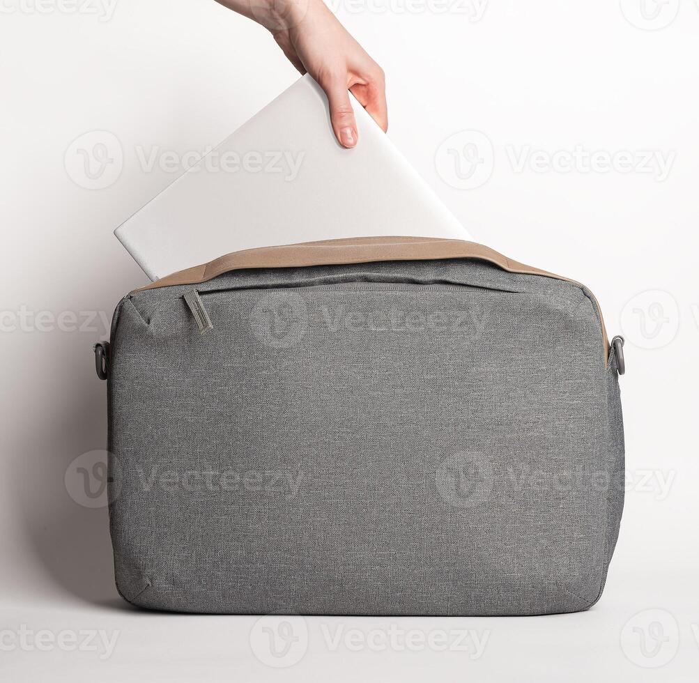 Hand putting laptop computer into notebook bag, briefcase photo