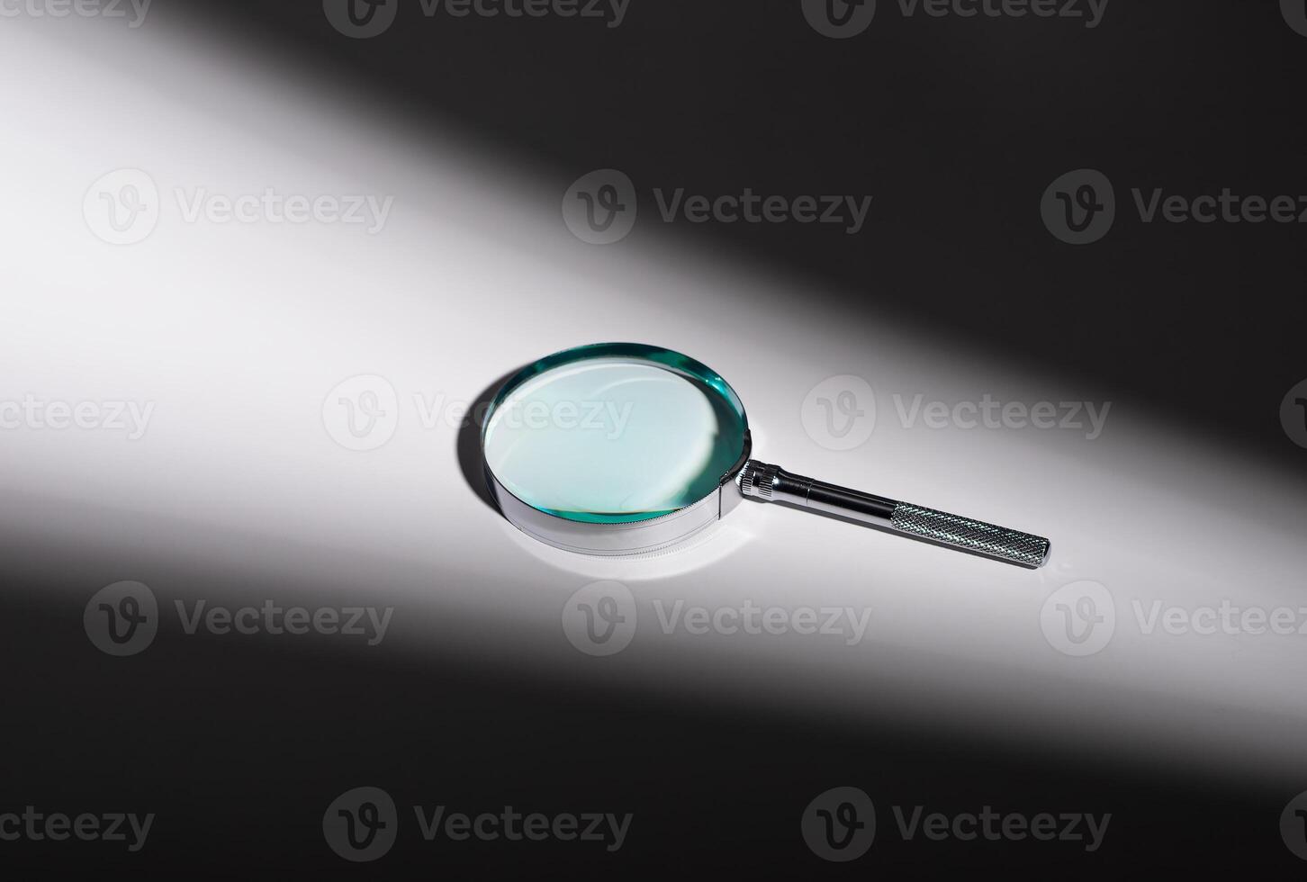 Silver magnifying glass on glass surface, shadow and light play. Optical zoom lens concept, photo