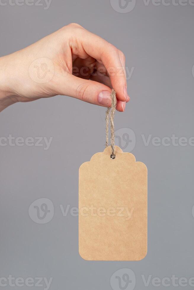 Hand holding paper price tag, gift label on cord, twine isolated on white background photo