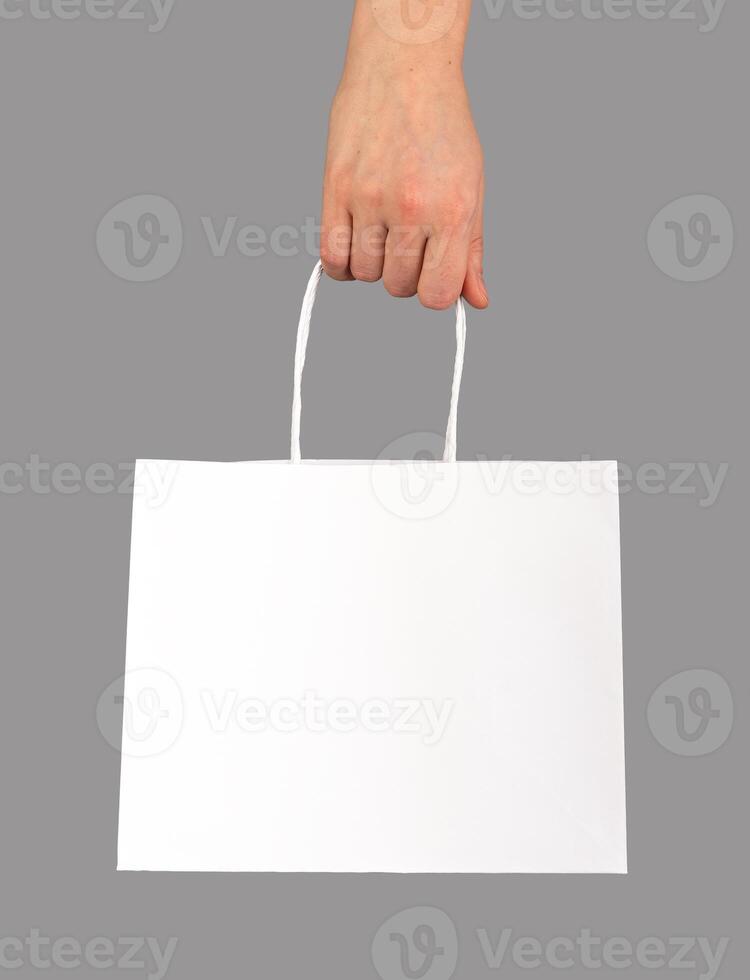 Hand holding shopping bag, paper packet, pack with handles, white package isolated photo