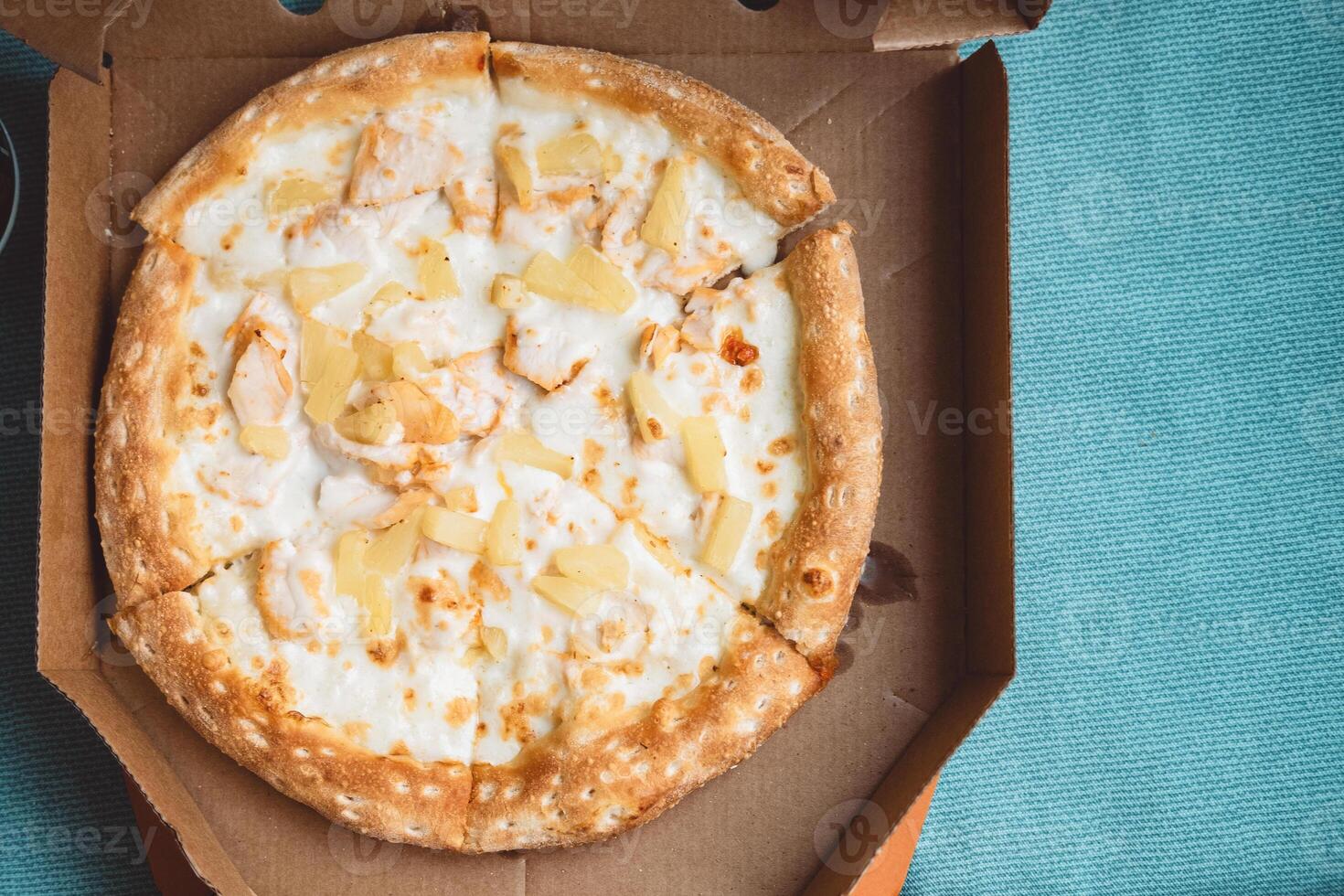 Delicious Italian pizza with pineapples and chicken meat in a box on a blue background photo