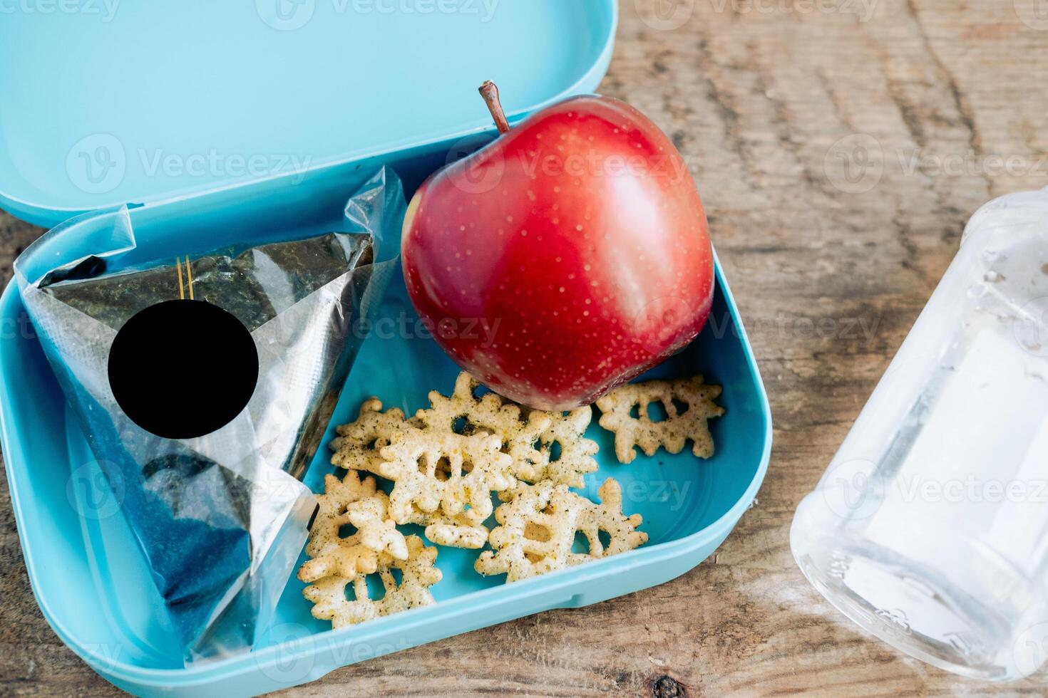 asiático estudiantes caja de almuerzo de onigiri, patatas fritas y manzana con botella de agua, en de madera antecedentes foto