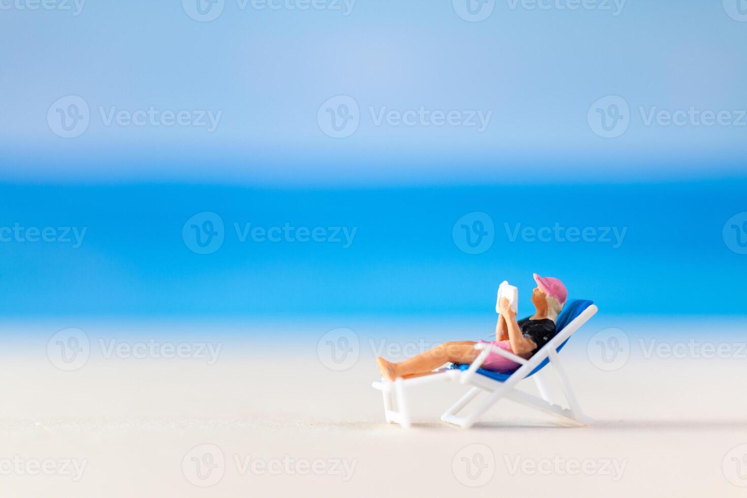miniatura personas , un mujer relajante en un cubierta silla y leyendo un libro foto