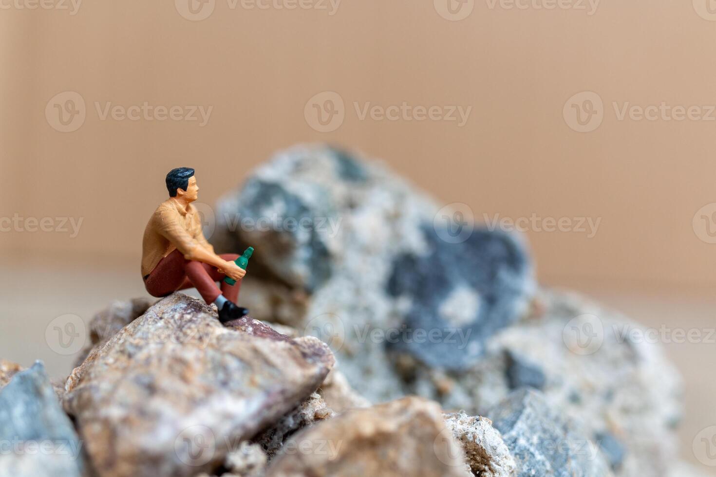 Miniature people , A young man sipping beer while sitting on the rock photo