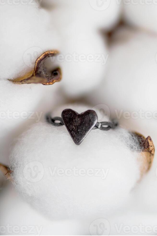 Elegant tiny handmade silver ring with heart on a background of cotton flowers. Jewelry accessories. photo
