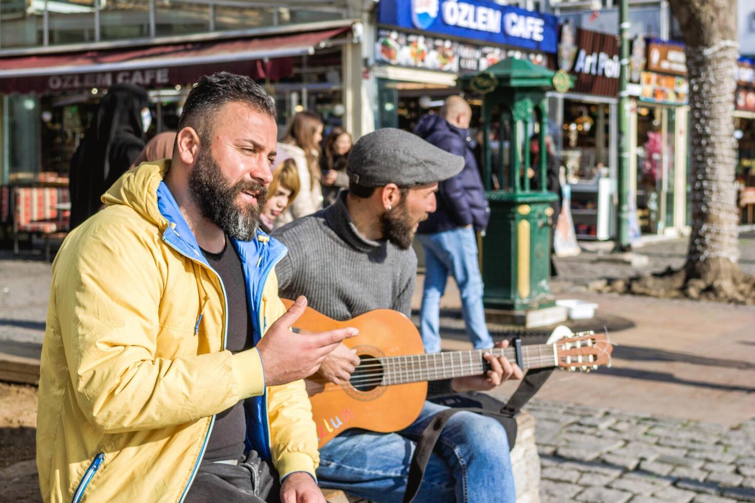 Istanbul, Turkey - December 29, 2022. Two men, one playing guitar and singing, the other listening intently on a city street corner. photo