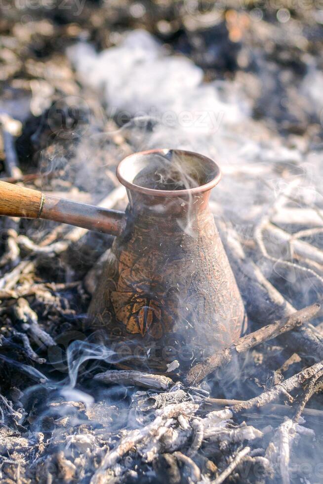 Making coffee in cezve on the bonfire when camping or hiking in the nature. Coffee on campfire. photo