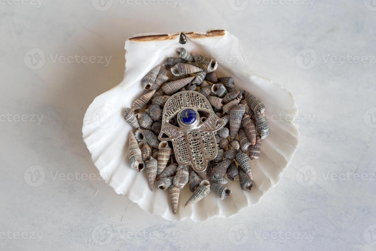 A stunning silver Hamsa hand featuring a mesmerizing blue evil eye charm, representing protection, displayed against a tranquil background of delicate white seashells. photo