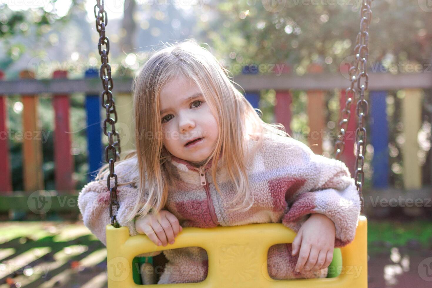 Adorable toddler girl playing on a swing set in a colorful playground. photo
