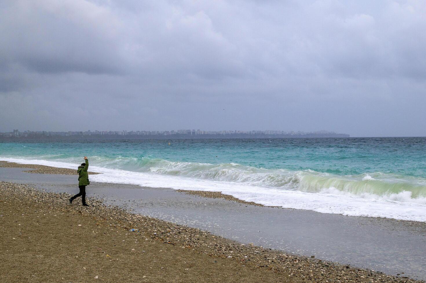antalya, Turquía - marzo 05, 2023. irreconocible hombre es caminando cerca a Tormentoso mar con grande olas y ciudad en antecedentes. foto