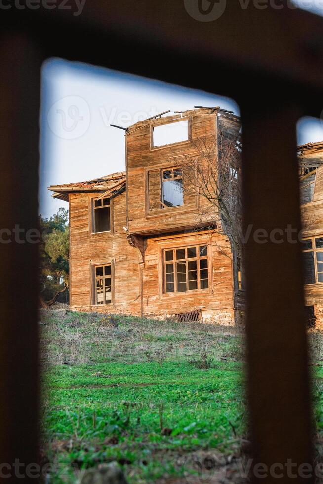 Wooden house with broken windows and a large yard overgrown with grass. photo