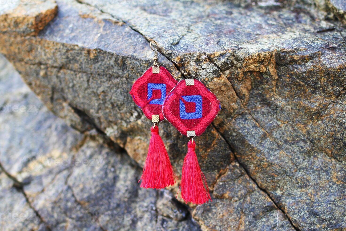 Colorful tribal design fashion handmade earrings from threads on a stones texture background. photo