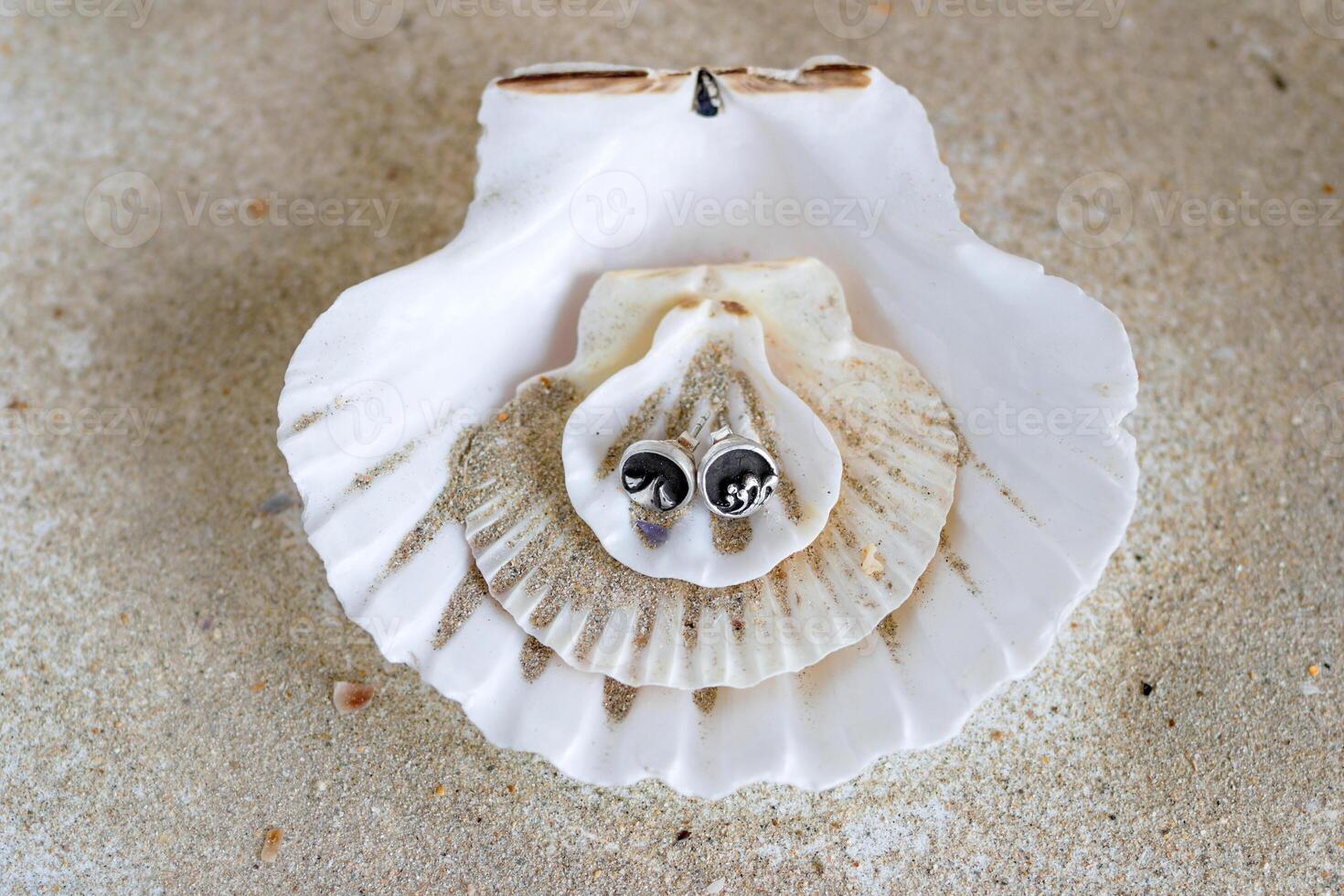 Pair of silver earrings on a background of seashells and sand. Handcraft precious item. Sea theme. photo