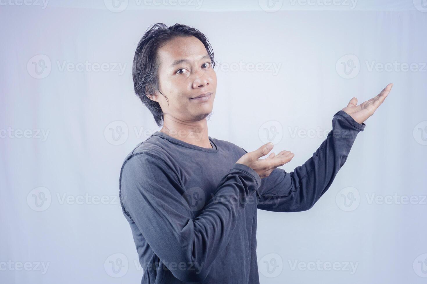 Handsome Asian man facing the camera is pointing at the copy space for advertising on an isolated white background. photo