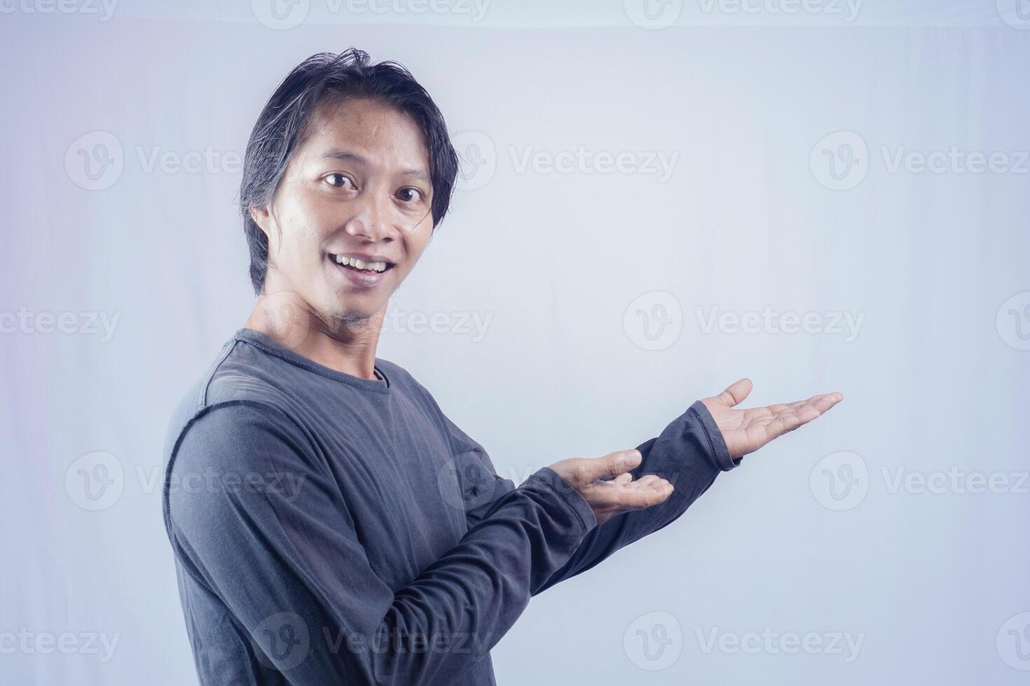 Handsome Asian man facing the camera is pointing at the copy space for advertising on an isolated white background. photo