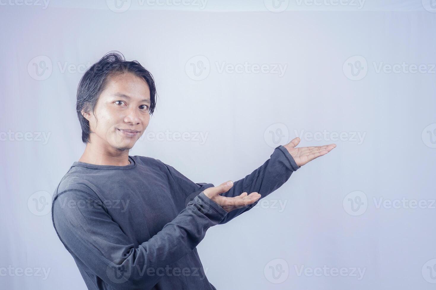 Handsome Asian man facing the camera is pointing at the copy space for advertising on an isolated white background. photo