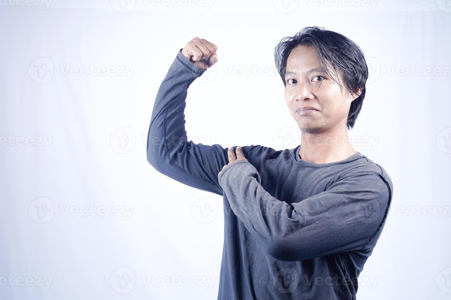 handsome asian man is cheering with raised hand to show his arm strength on isolated white background for copy space photo