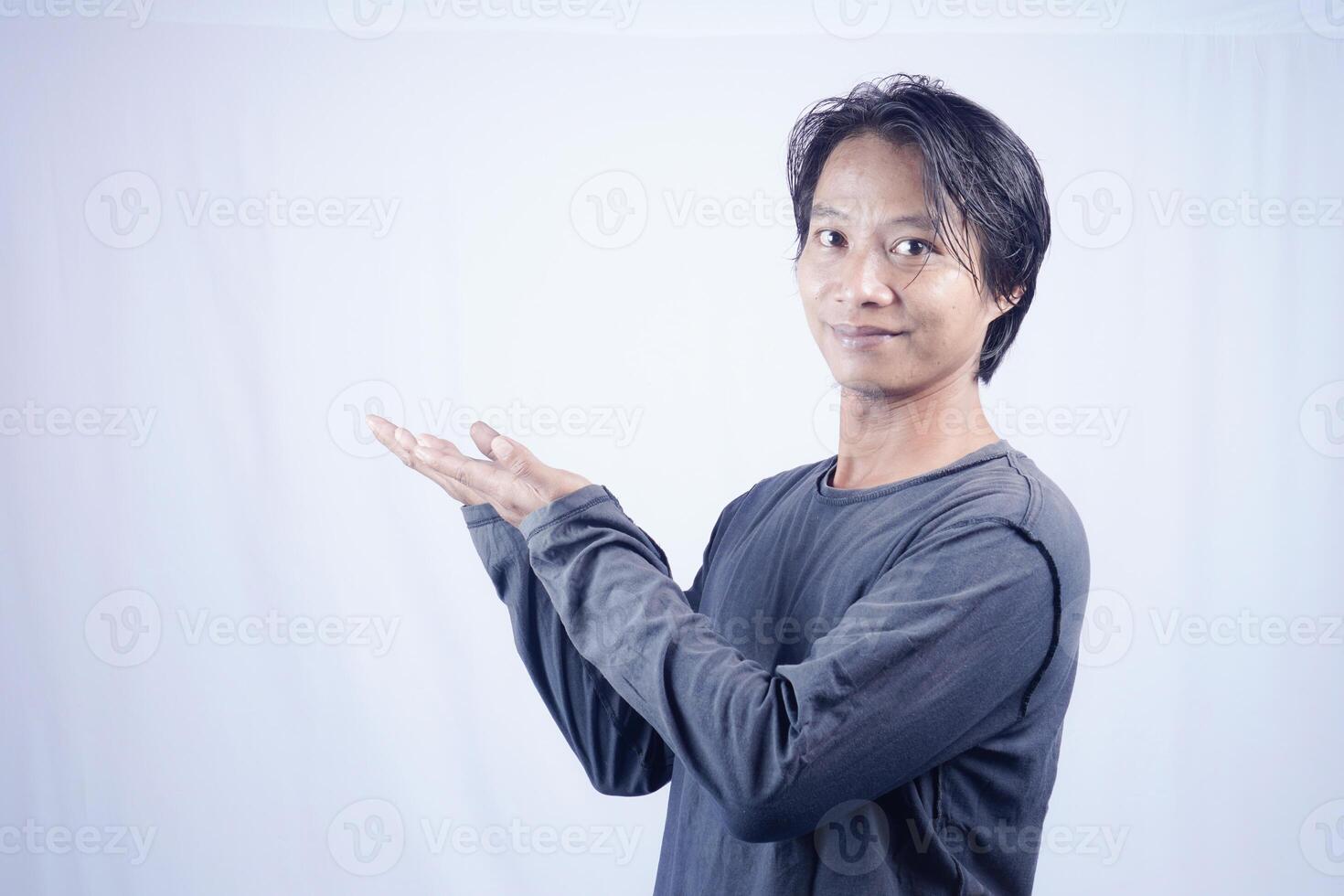 Handsome Asian man facing the camera is pointing at the copy space for advertising on an isolated white background. photo