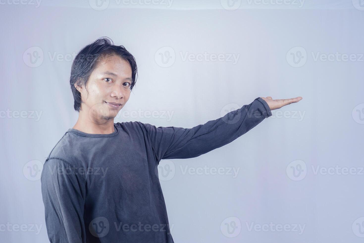 Handsome Asian man facing the camera is pointing at the copy space for advertising on an isolated white background. photo