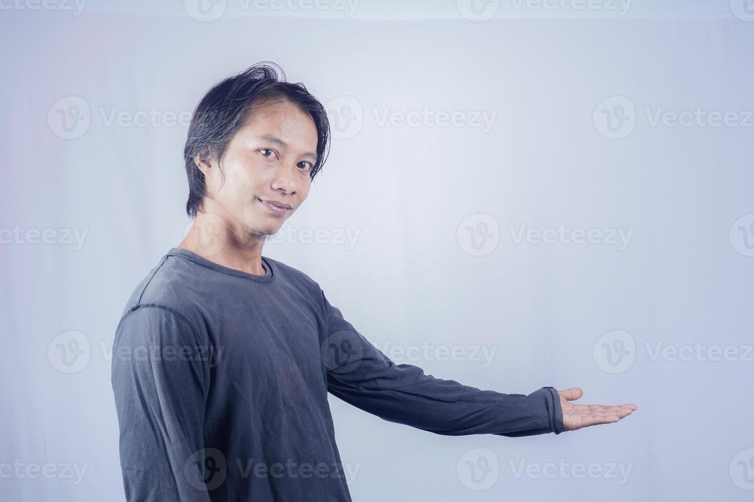 Handsome Asian man facing the camera is pointing at the copy space for advertising on an isolated white background. photo