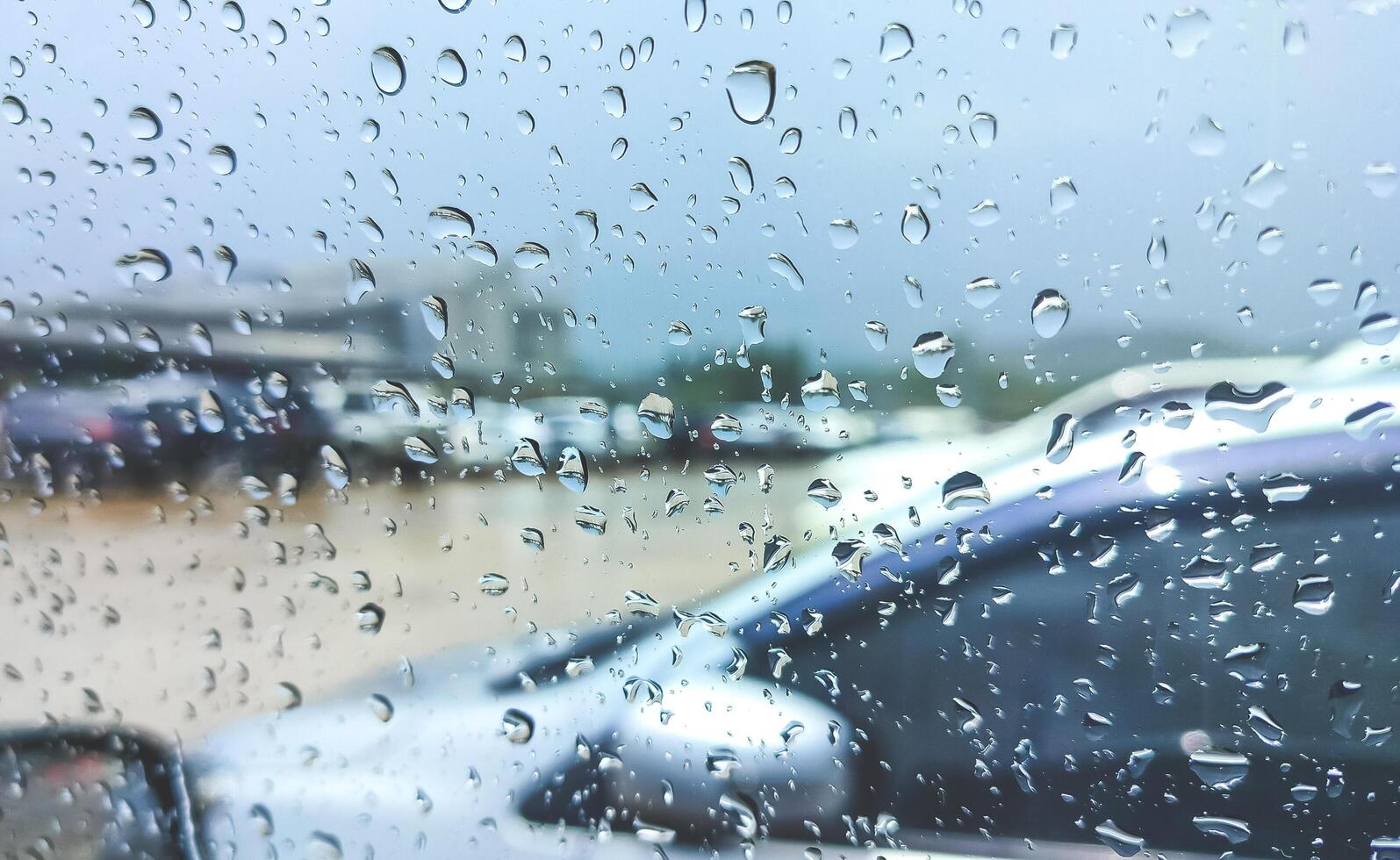 Rain drops on car glass window surface of driver's door while parked in outdoors parking lot during rainy weather photo