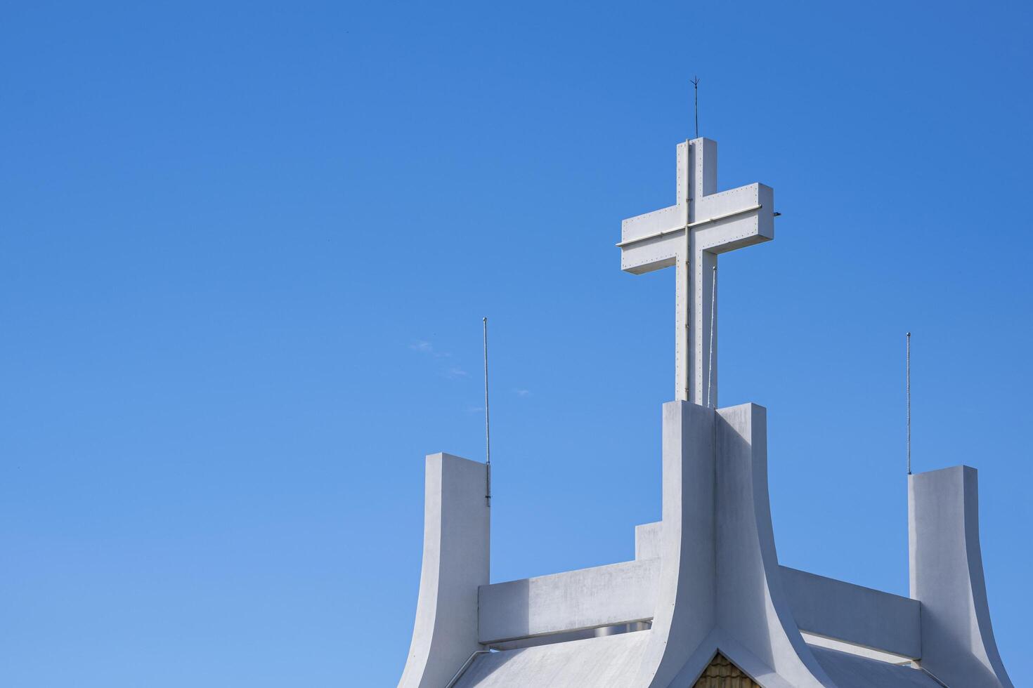 Low angle view of large cross on rooftop of white church against blue sky background photo