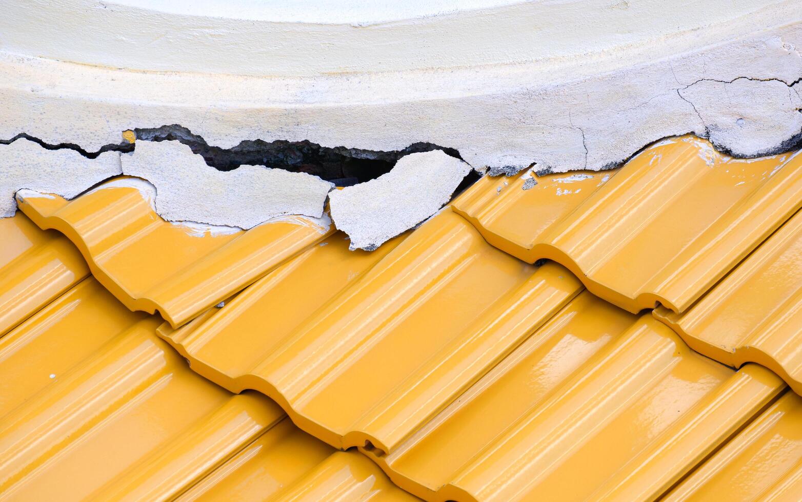 Crack and broken texture of damaged white concrete roof ridge with yellow ceramic tile roof photo