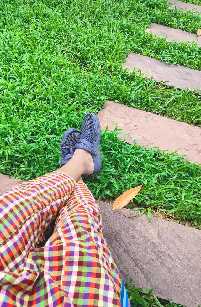 Part of man's legs in colorful plaid trousers with cross-legged gesture resting on bench in rest area at public park, top view with copy space photo