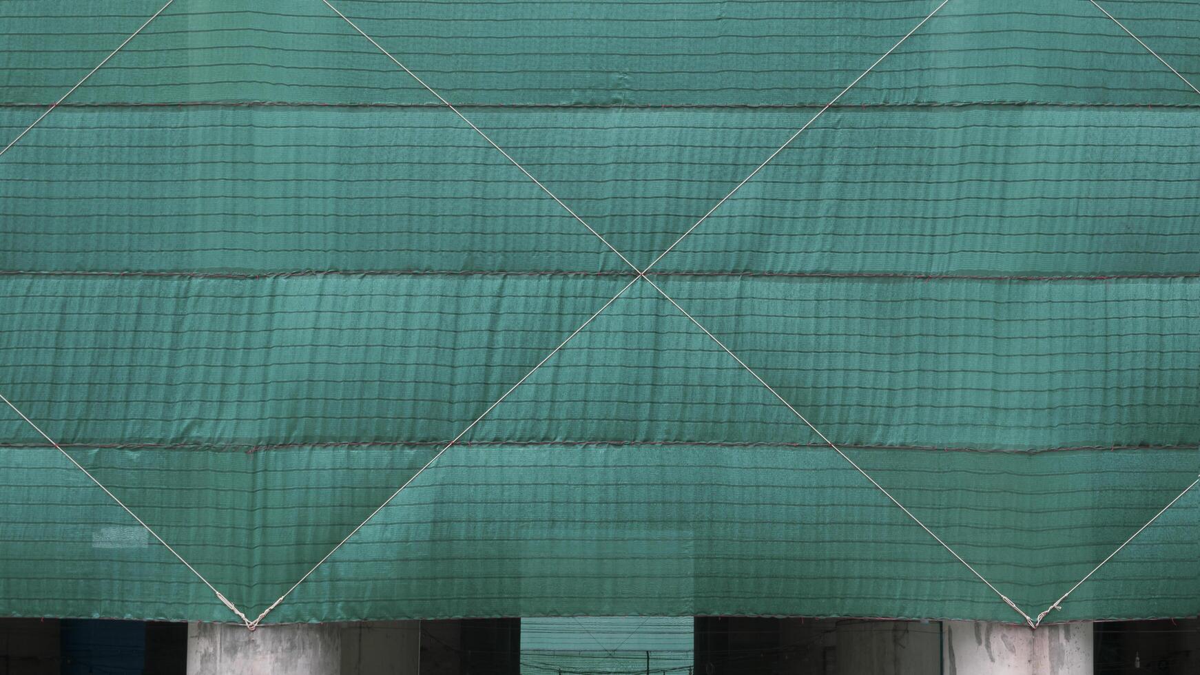 Front view of green mesh sheets covering column of large building in construction site area photo