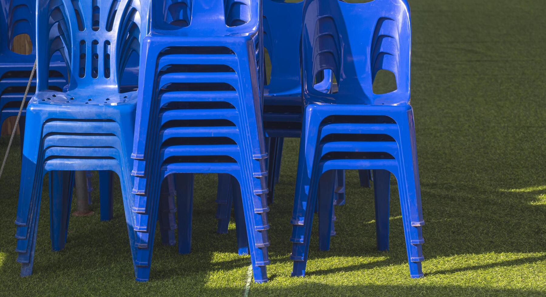 Many stack of blue plastic chair on green artificial turf for outdoors event photo