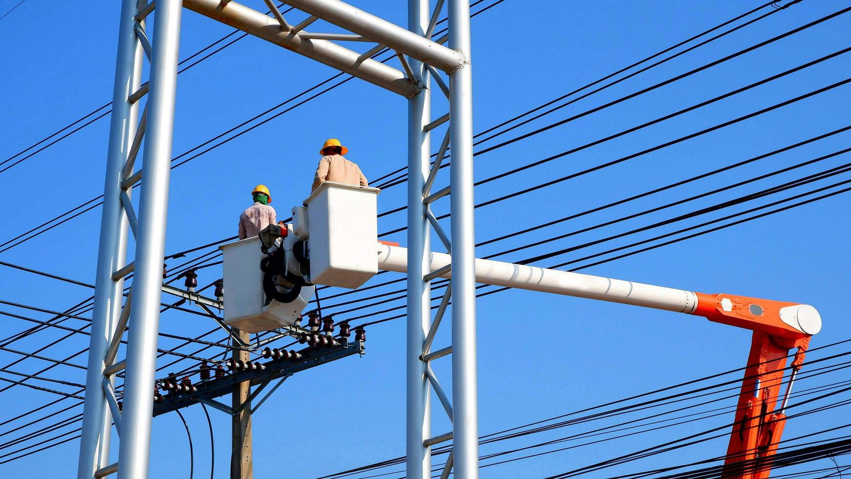 dos electricistas en Cubeta auge camión son instalando eléctrico sistema en poder polo en contra azul claro cielo antecedentes foto