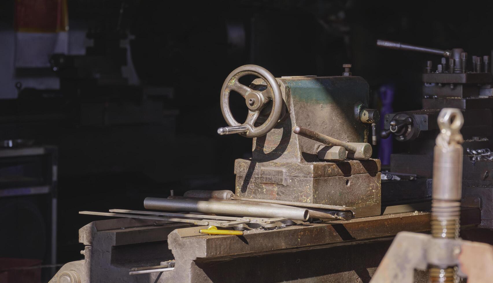 Sunlight and shadow on surface of the old metal turning lathe with work tools on dark background inside of mechanical workshop photo