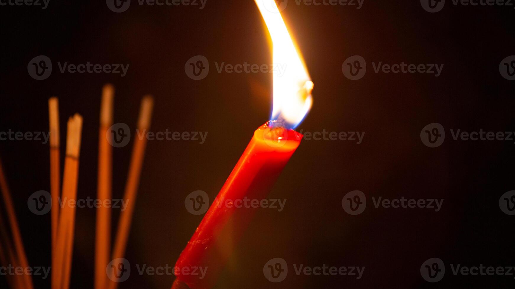 Burning red candle and incense smoke with black background photo