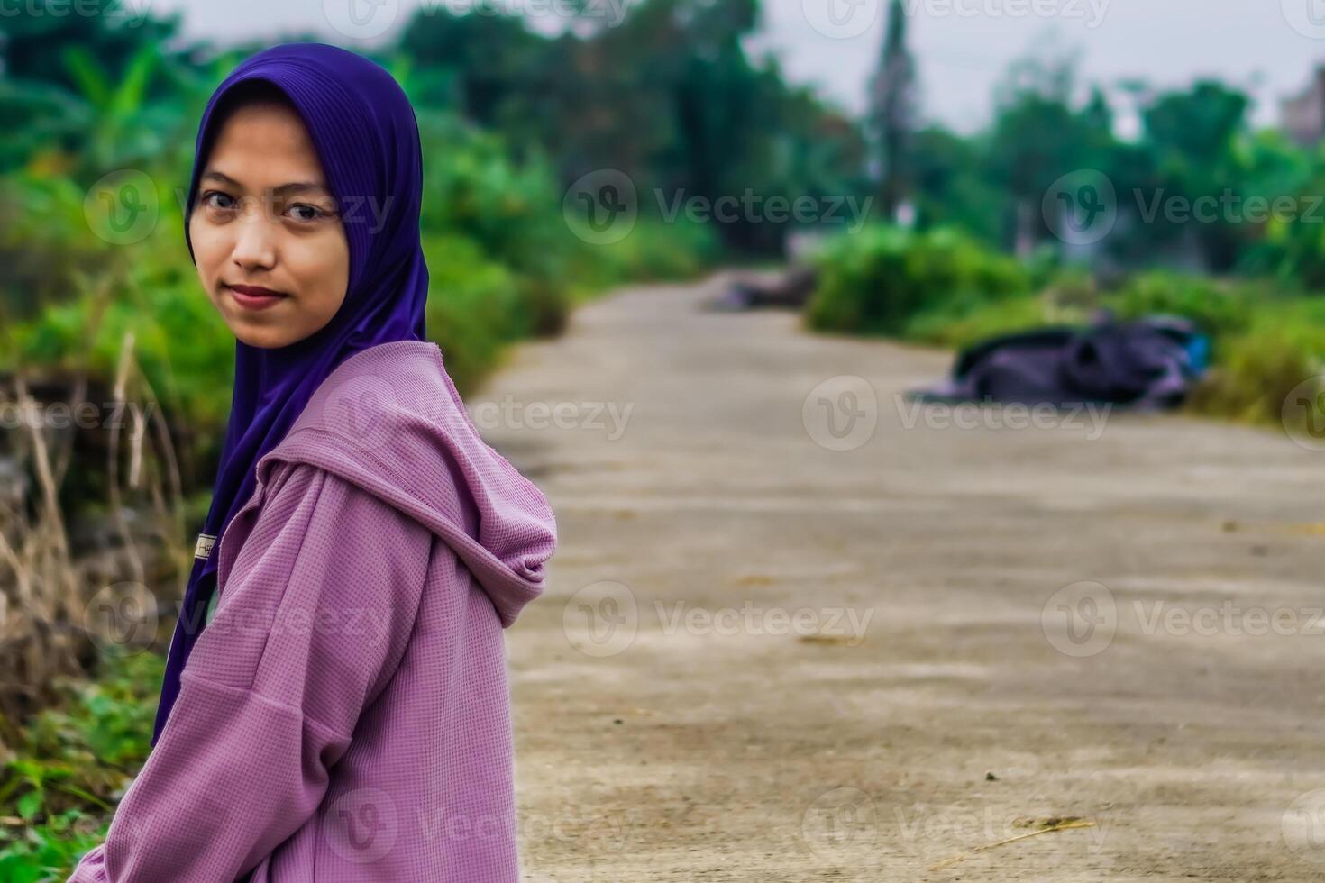 side view of a woman wearing a headscarf sitting beside a rice field road in the morning. photo